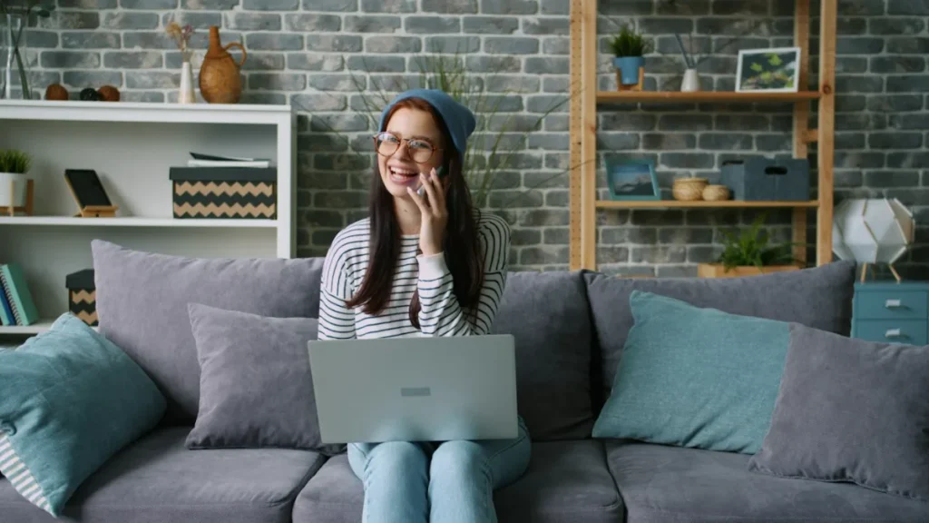 Smiling woman talking on the phone with a laptop on the couch after opting out of AmericaPhonebook