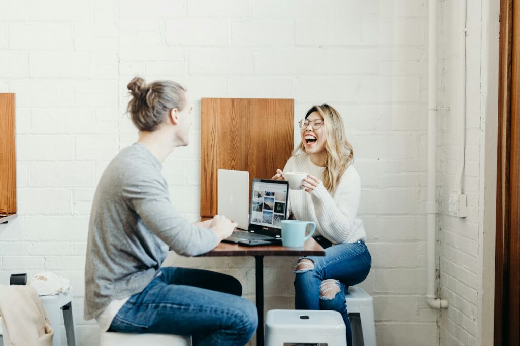 Two people laughing together at a table with a laptop