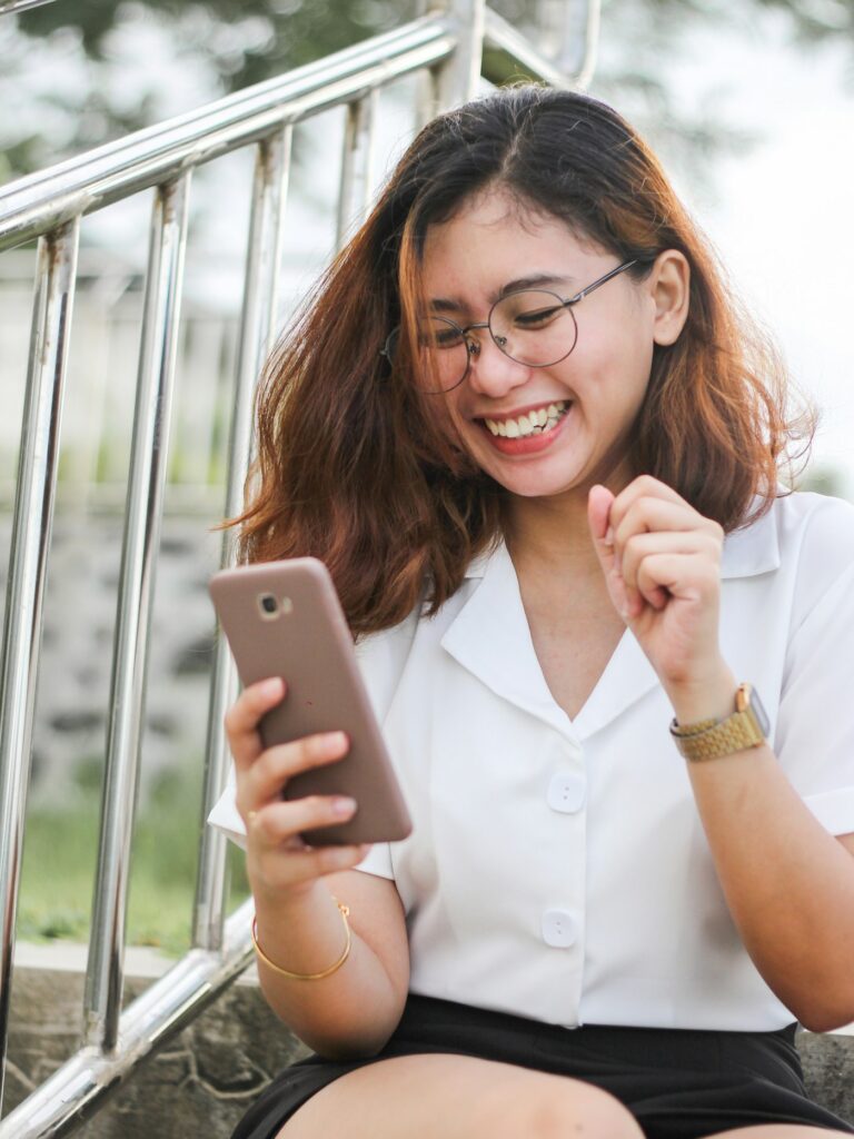 Woman in a white shirt laughing while looking at her phone