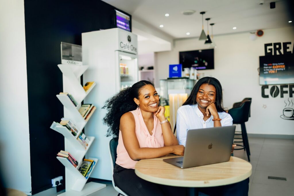 Two smiling women sitting at a table with a laptop