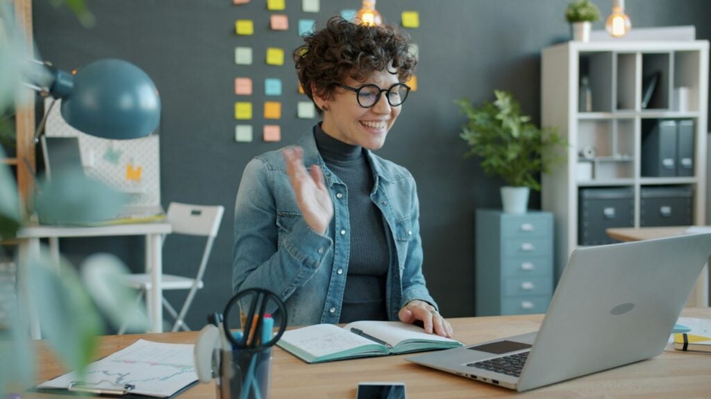 Smiling woman waving during a video call at her desk